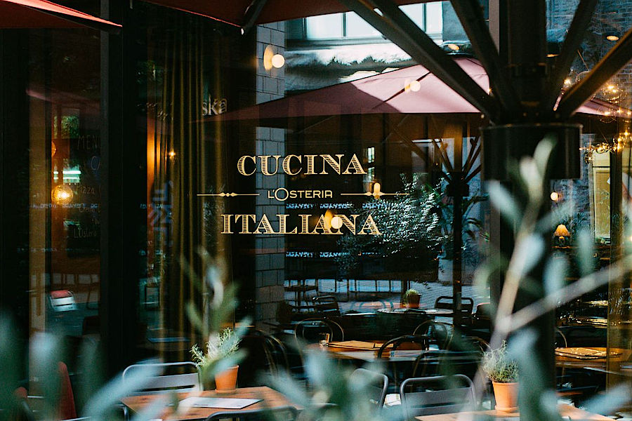 Außenansicht der L’Osteria Berlin‑Mahlsdorf mit Terrasse und aufgebauter Eisstockbahn im Vordergrund, geeignet als Veranstaltungsort für Eisstockschießen bei einem Teamevent oder einer Weihnachtsfeier